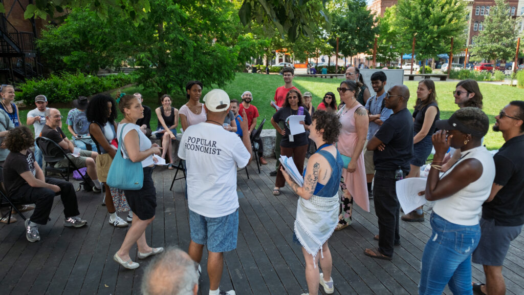 Summer Institute facilitators leading a discussion amongst seated and standing participants in Pulaski Park, Northampton