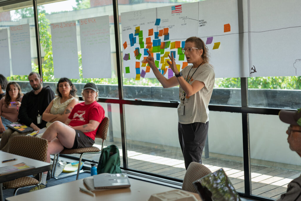 A Summer Institute participant presenting rapid research in front of a canvas covered with sticky notes